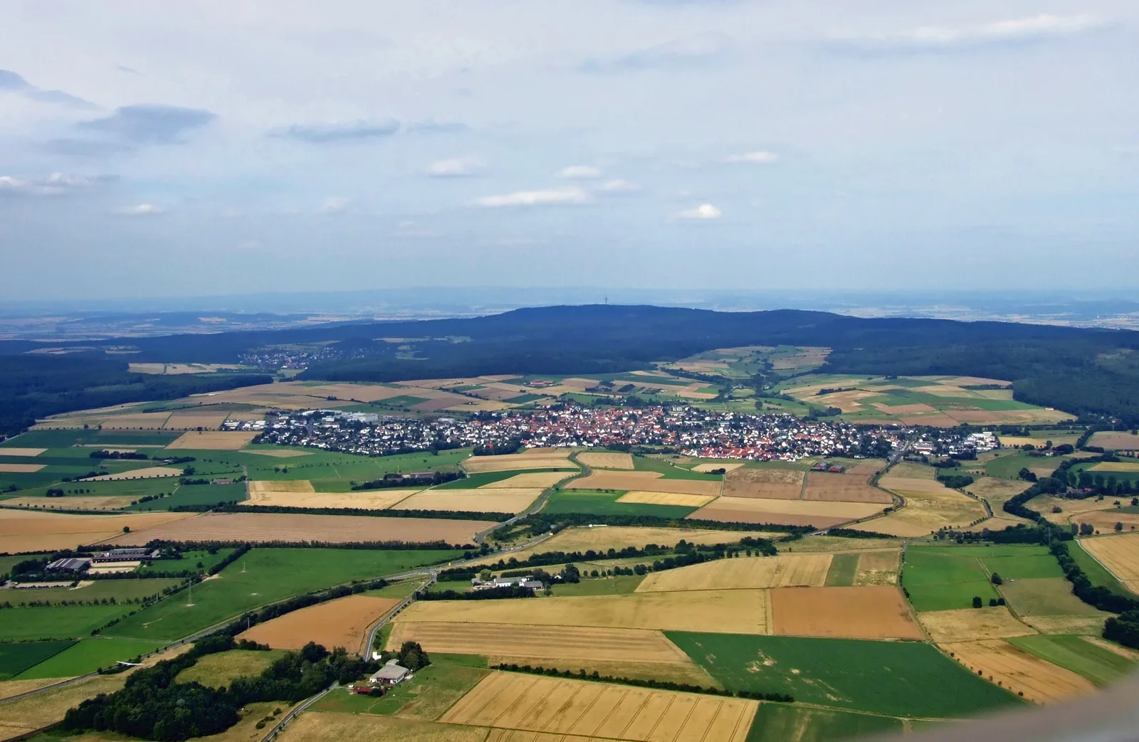 Luftaufnahme von Wehrheim zwischen Feldern, dahinter die bewaldeten Höhen des Taunus